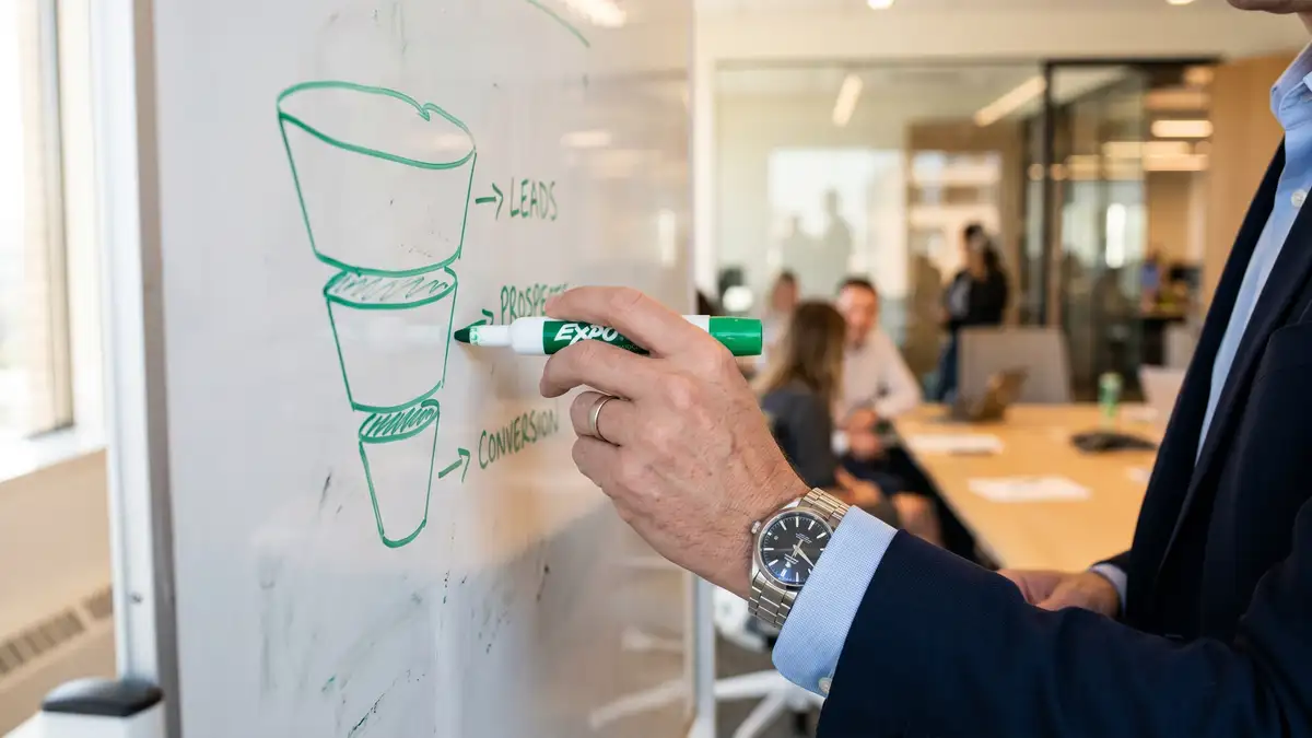 Executive's hands sketching a dual-funnel demand-gen and lead-gen diagram on a whiteboard with green marker during a strategy session