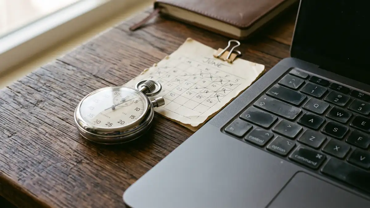 A stopwatch and a paper calendar page beside a laptop keyboard marking a ninety-day measurement window