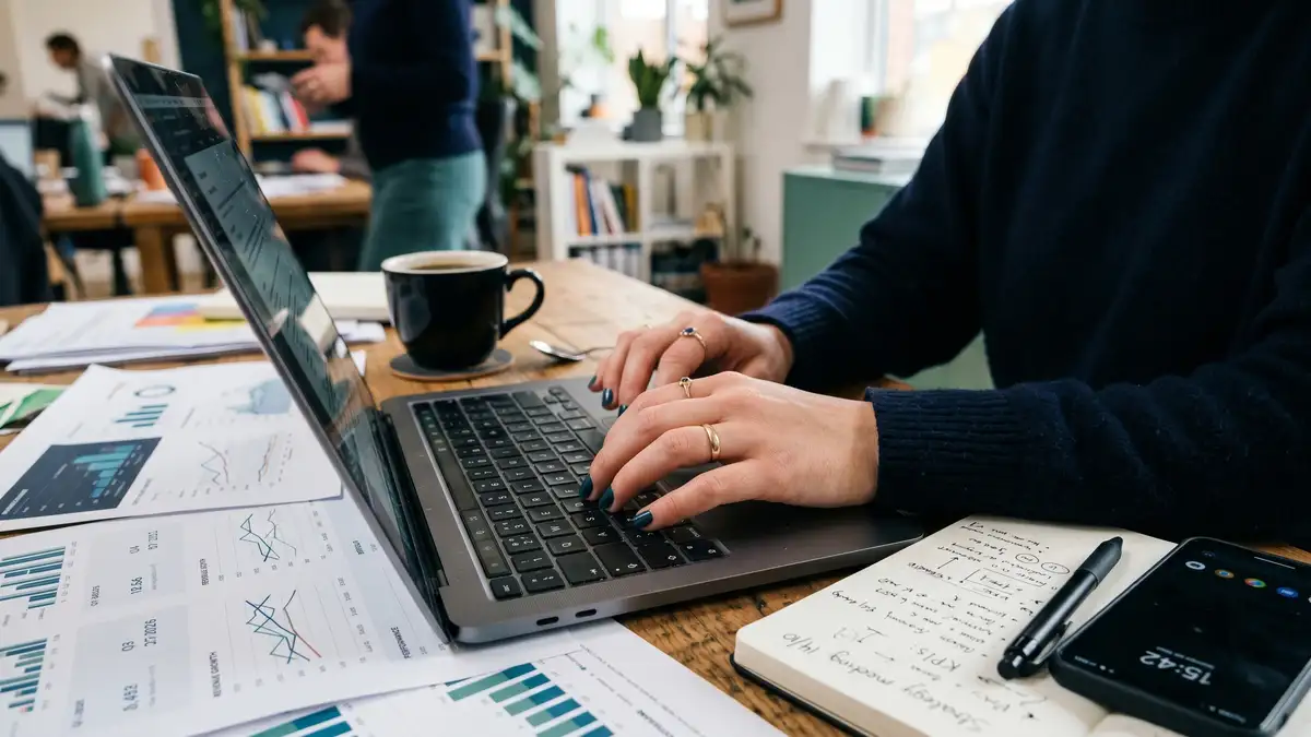 Hands on a laptop at a desk covered with analytics dashboards
